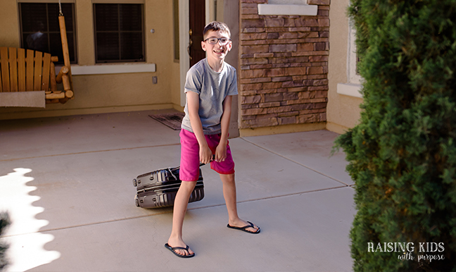 boy with suitcase in front of house