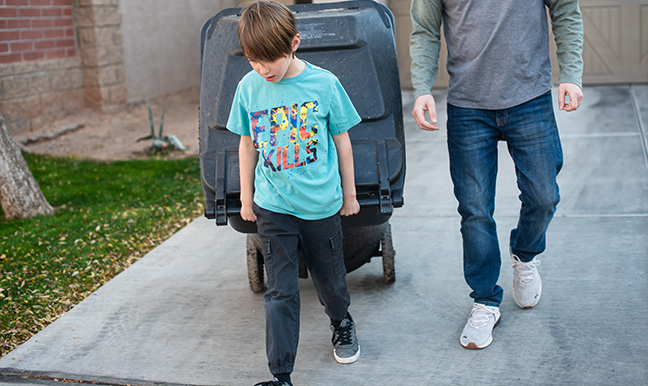 boy carrying garbage can out to street with dad