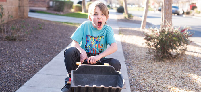 crazy kid riding digger toy down the sidewalk