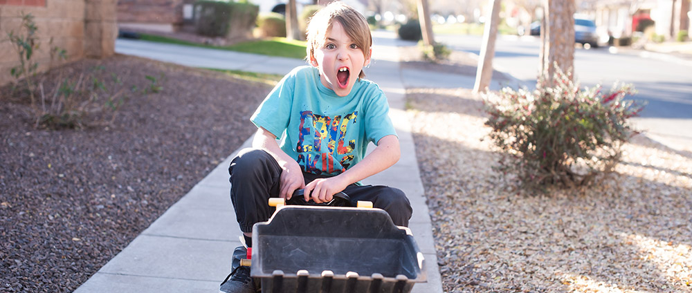 crazy kid riding digger toy down the sidewalk